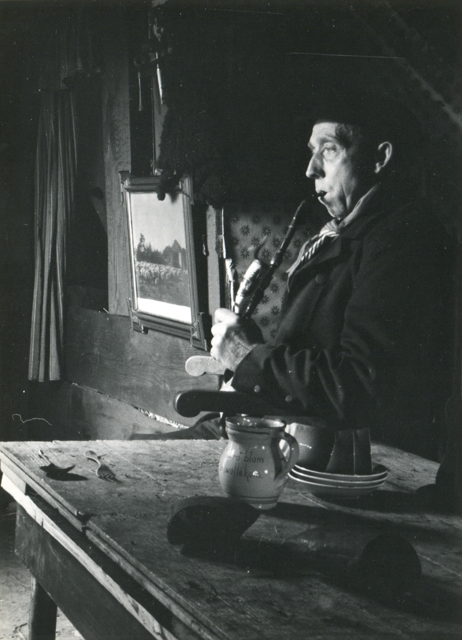Pijprokende man in een plaggenhut in openluchtmuseum Schoonoord, 1954 (zwart-wit foto)